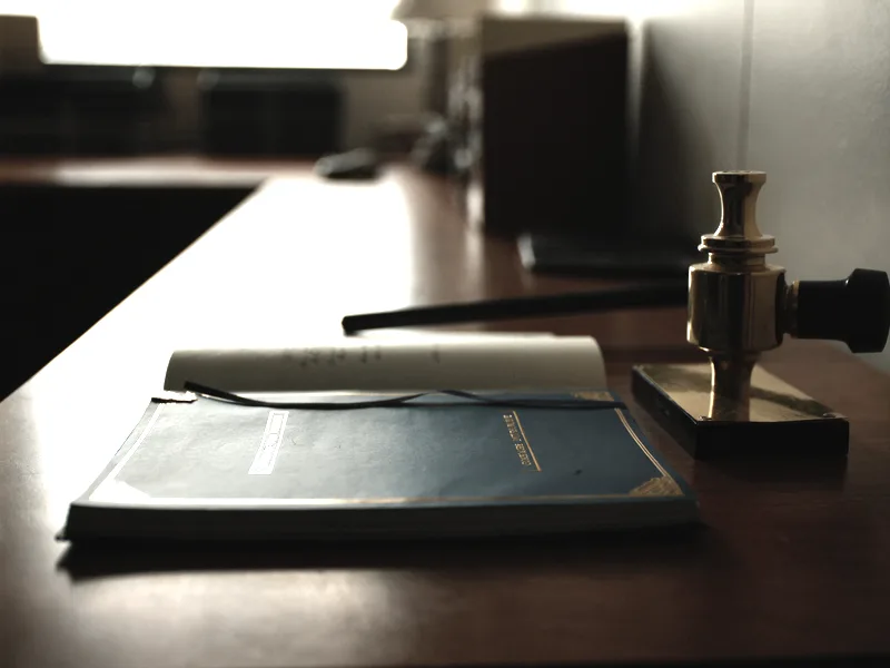 A corporate minute book with a ribbon bookmark beside a brass seal embosser