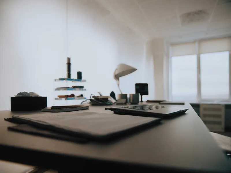 A laptop and document folio on a desk beside a bright window