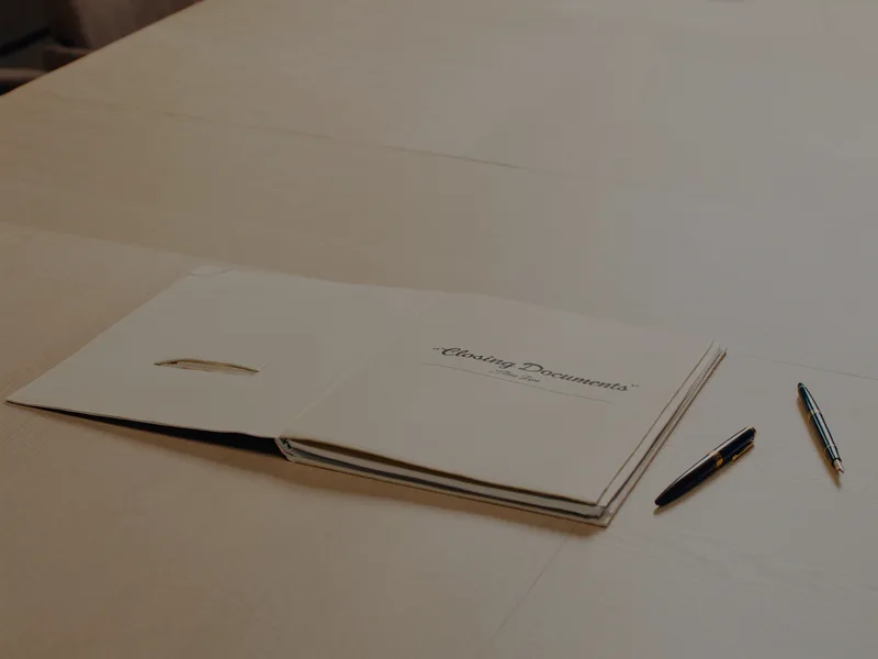 A closing documents folio with two fountain pens on a boardroom table